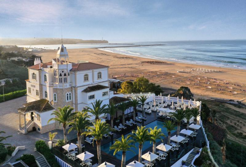 The image shows a spooky place in Portugal. It is an hotel, facing the beach. The weather is sunny with a clear sky.